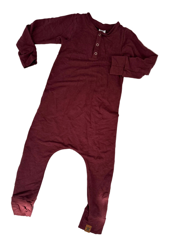 A burgundy long-sleeve one-piece jumpsuit with a three-button henley neckline, laid flat on a white surface with dappled shadows.
