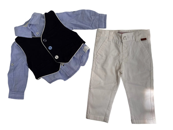 A children's clothing set laid flat on a light surface, including a light blue long-sleeve shirt, a navy vest with white trim and buttons, and off-white pants.