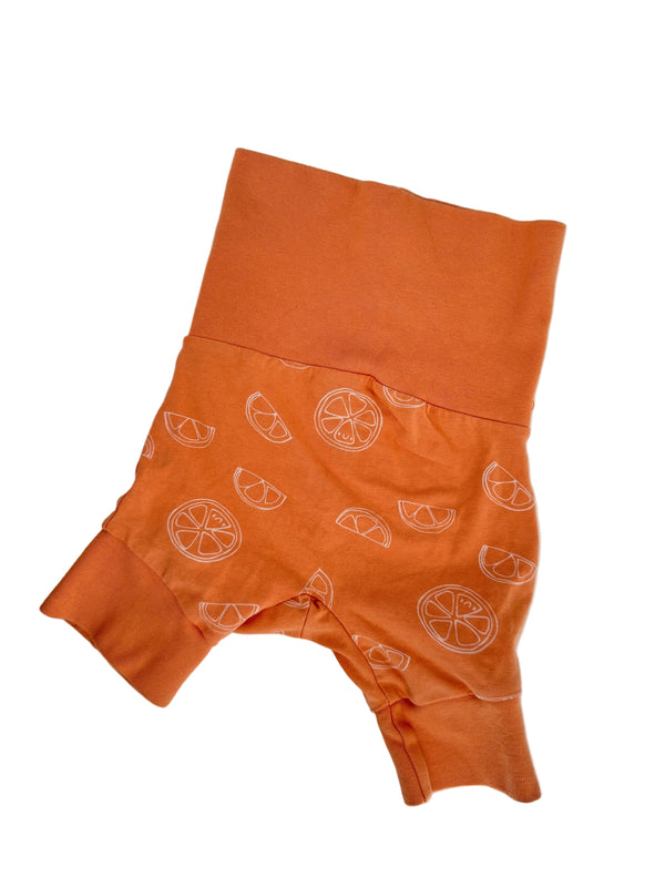 An orange baby romper with white citrus slice patterns, laid flat on a light gray marble surface.