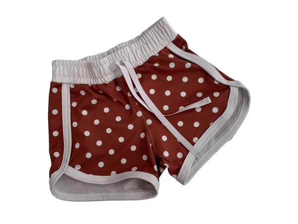Red and white polka dot athletic shorts with a white elastic waistband and white drawstring, laid flat on a light gray surface.