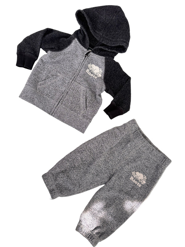 A baby clothing set laid flat on a light surface, including a zip-up hoodie and jogger pants. The hoodie is heather gray with black sleeves and hood, and the pants are heather gray with a small white embroidered logo on the thigh.