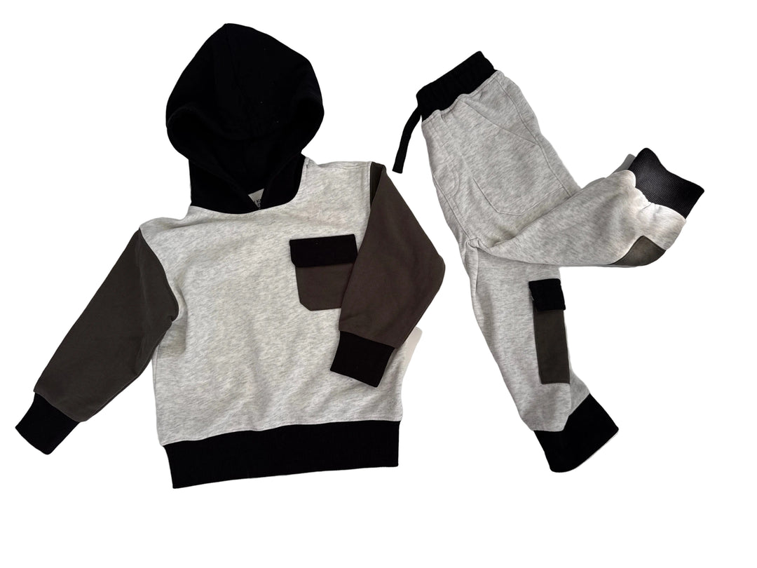 A two-piece children's sweatshirt and jogger set laid flat on a white surface. The hoodie has a light heather gray body, black hood and hem, dark brown sleeves, and a matching dark brown chest pocket.