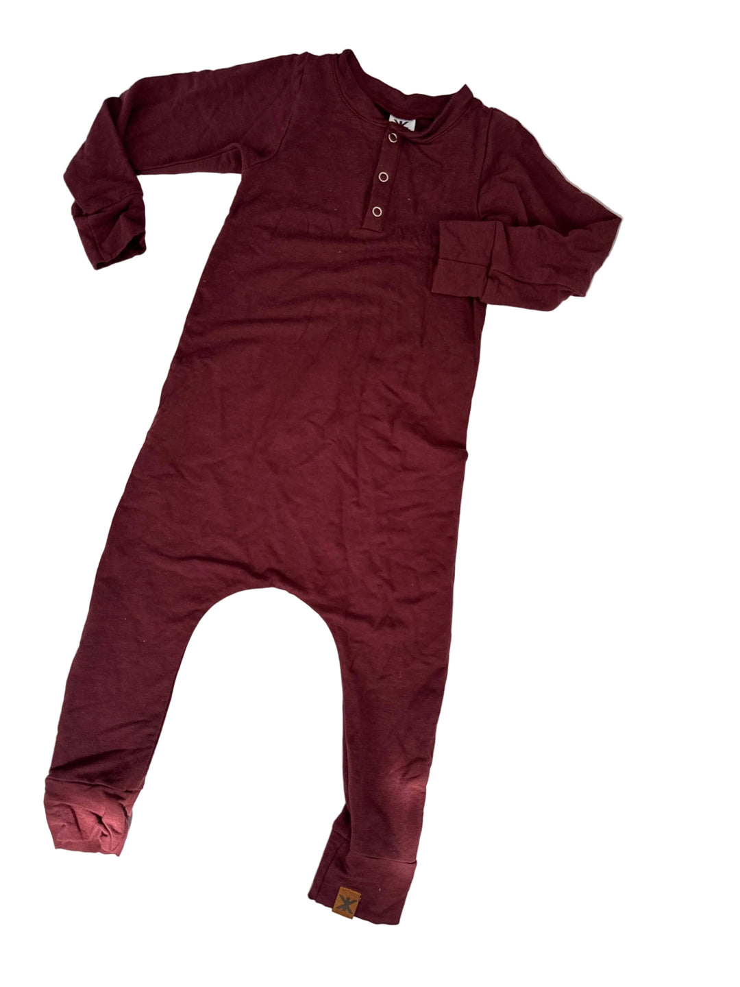 A burgundy long-sleeve one-piece jumpsuit with a three-button henley neckline, laid flat on a white surface with dappled shadows.