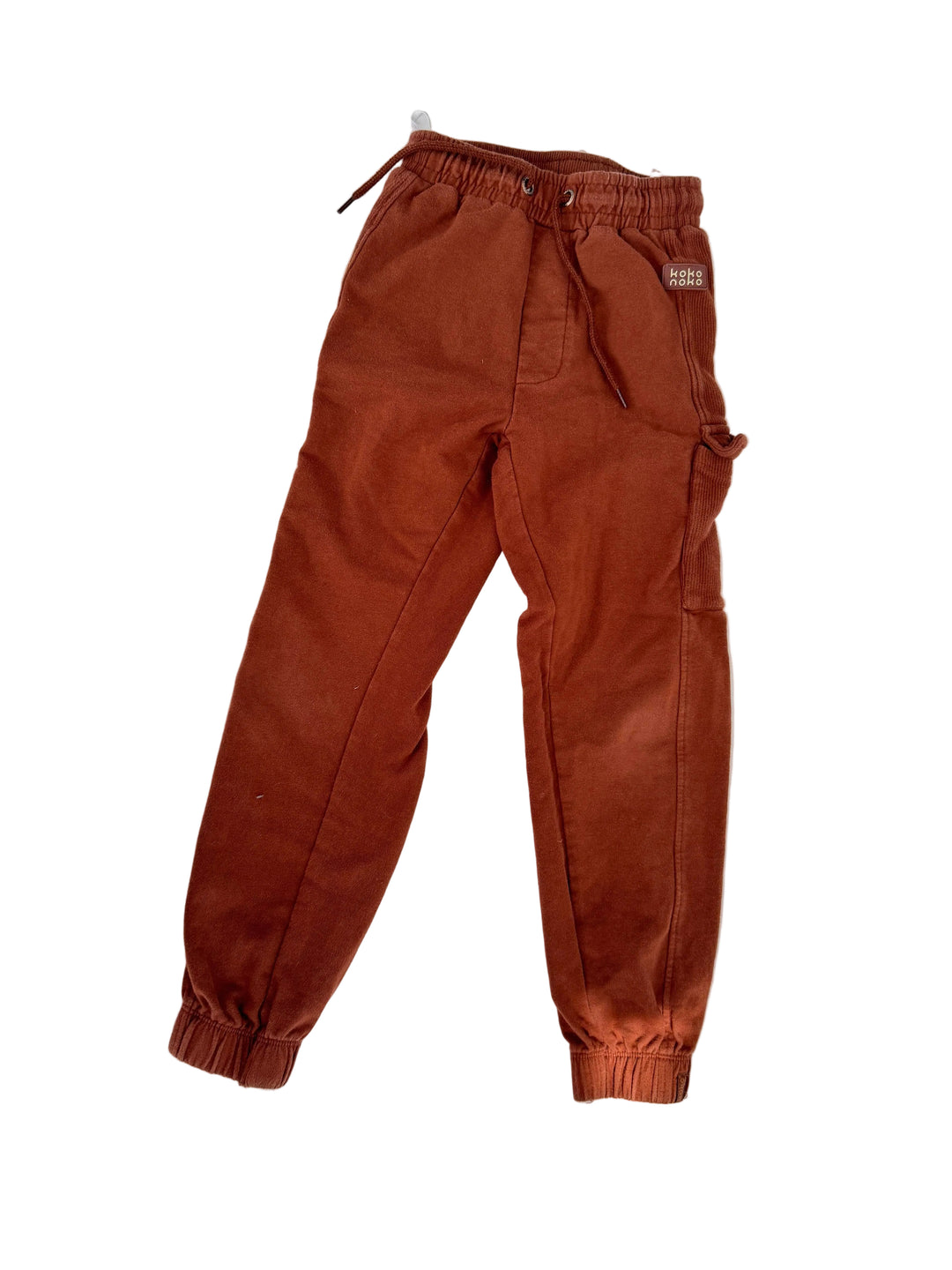 A pair of rust-brown jogger pants laid flat on a white surface with soft dappled shadows.