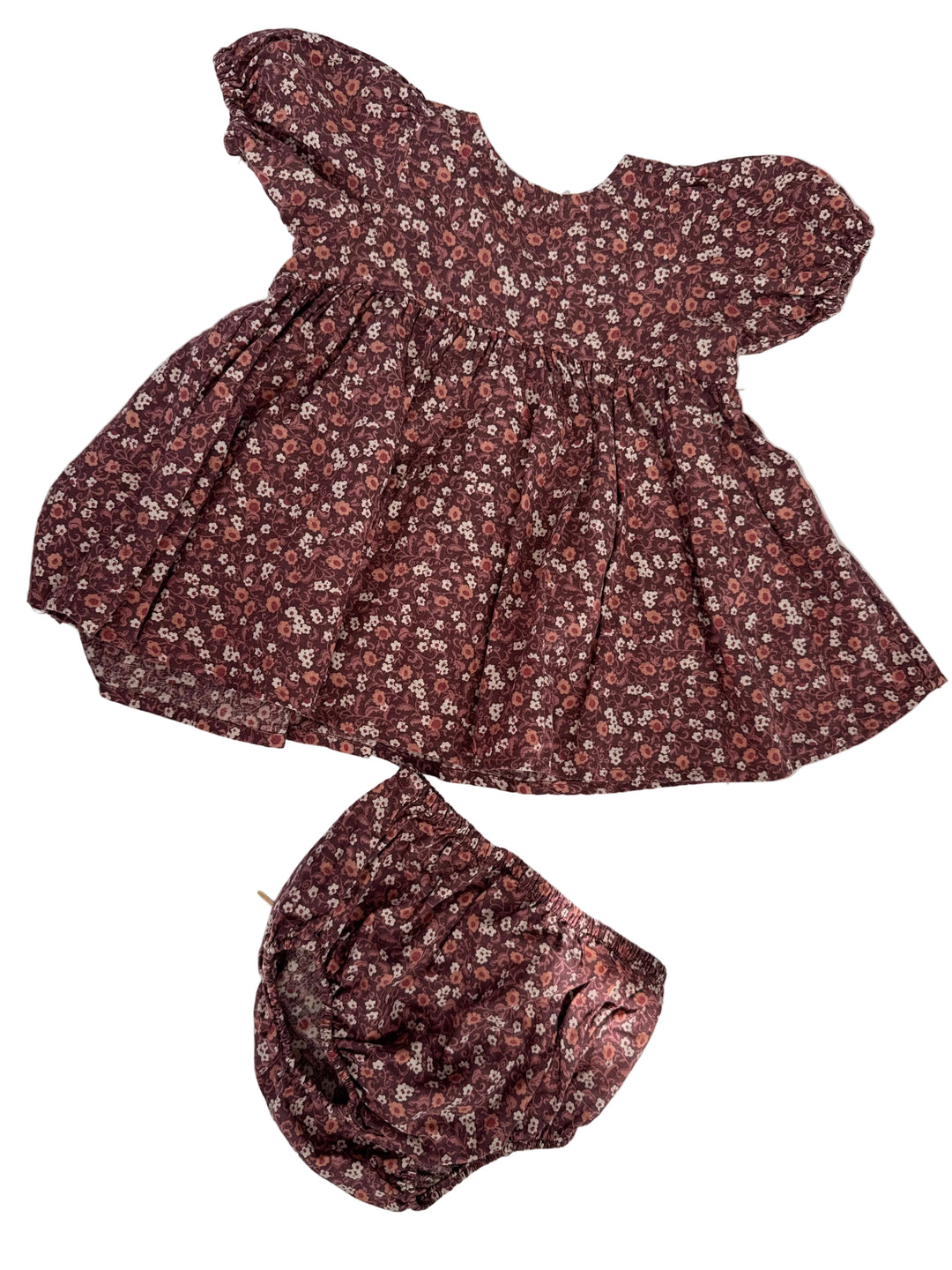 A matching two-piece clothing set consisting of a short-sleeve puff-sleeve top and a coordinating bonnet, both featuring a dense small floral print in dark reddish-brown, pink, and white, laid flat on a white surface with dappled shadows.