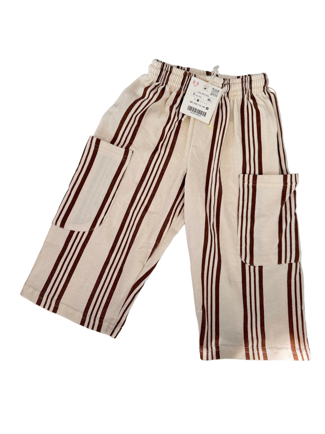 A pair of wide-leg linen pants in cream with dark brown stripes, laid flat on a light gray surface with soft leaf shadows.