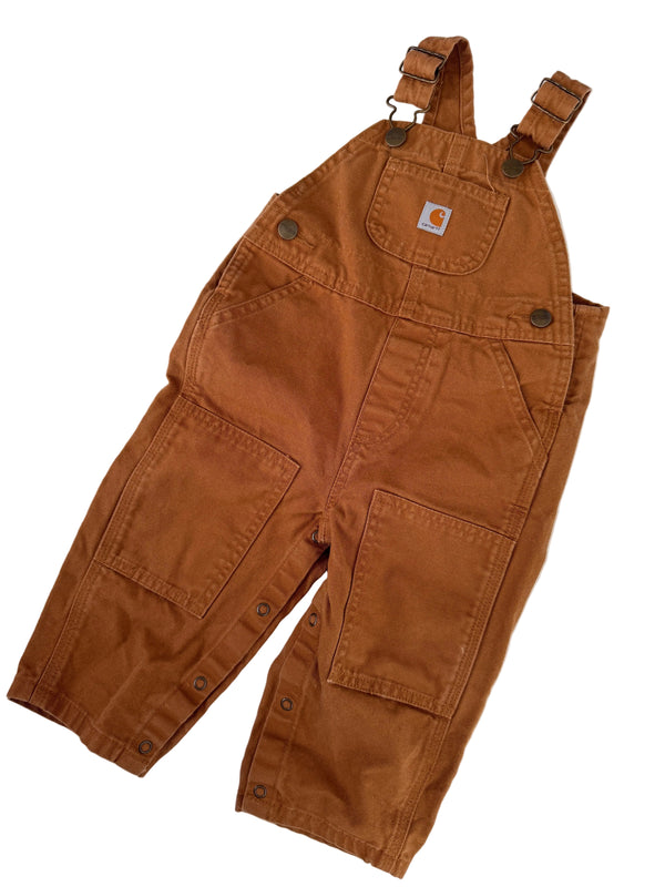 A pair of brown Carhartt bib overalls laid flat on a white background, featuring adjustable shoulder straps, front patch pockets, and button details.